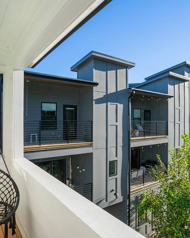 Balcony with hanging chair overlooking modern multi-unit property under blue sky
