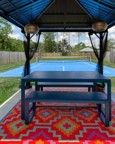 Covered pavilion with ping-pong table overlooking blue tennis court in fenced backyard