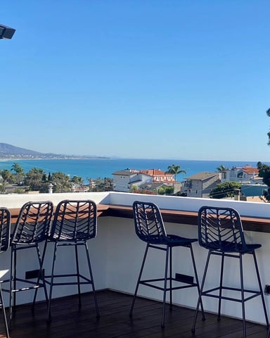 Rooftop deck with black bar stools overlooking coastal town and blue ocean bay