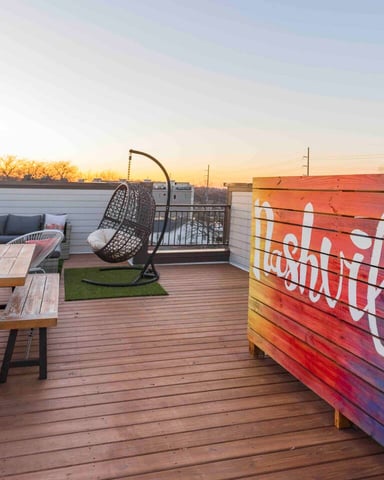 Rooftop deck with wooden table, hanging chair, seating area, and colorful painted wall at sunset