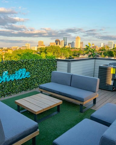 Rooftop lounge with gray seating, artificial turf, and city skyline view at sunset