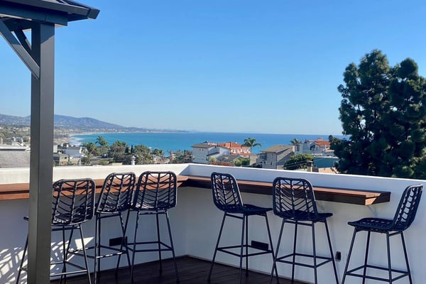 Rooftop deck with black bar stools overlooking coastal town and blue ocean bay