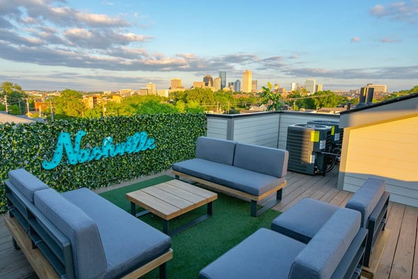 Rooftop lounge with gray seating, artificial turf, ivy-covered wall, and city skyline view at sunset