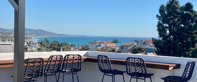 Rooftop deck with black bar stools overlooking coastal town and blue ocean bay