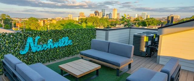 Rooftop lounge with gray seating, artificial turf, ivy-covered wall, and city skyline view at sunset