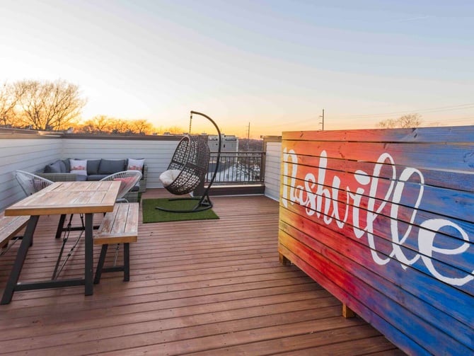 Rooftop deck at sunset with wooden table, hanging chair, seating area, and colorful painted wall at dusk
